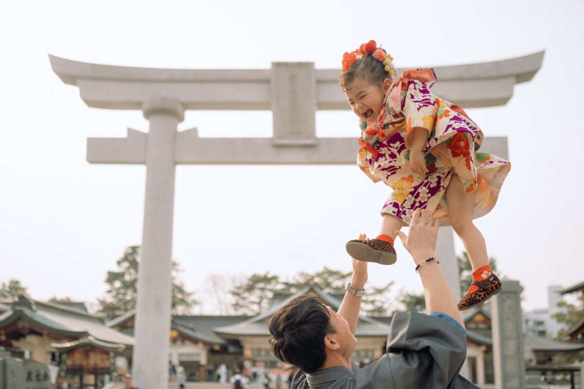 広島護国神社の鳥居前で、晴れ着姿のお子さんを父親が高く抱き上げる出張ロケーション撮影