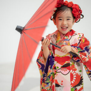 広島市安佐南区・十色写真STUDIOで撮影した7歳の七五三。色鮮やかな着物姿の女の子が赤い和傘を肩にかけ、自然な笑顔を見せている